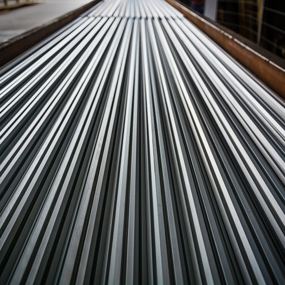 Rzędy ułożonych pionowo arkuszy blachy trapezowej w hali magazynowej.